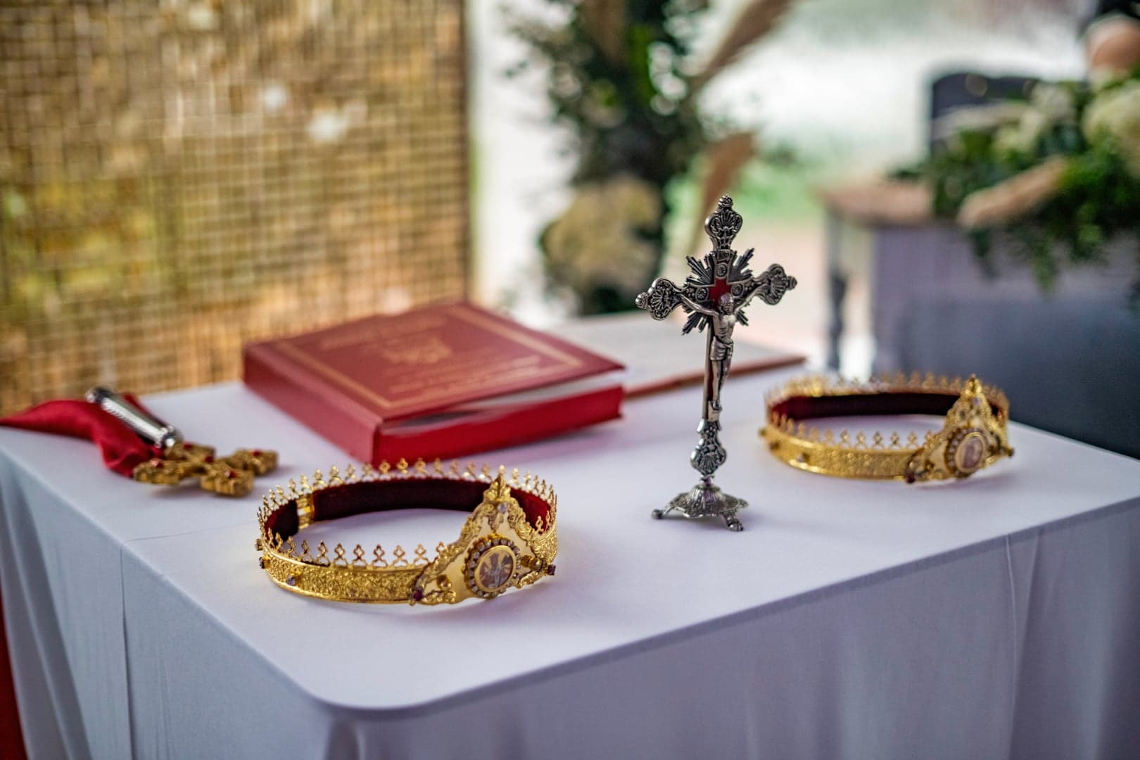 Twee gouden orthodoxe trouwkronen en een zilveren kruis op een ceremonietafel.