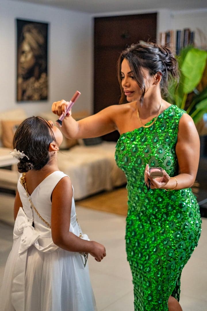 Sara Dera in een smaragdgroene jurk helpt een jong bruidsmeisje met make-up voor de ceremonie.