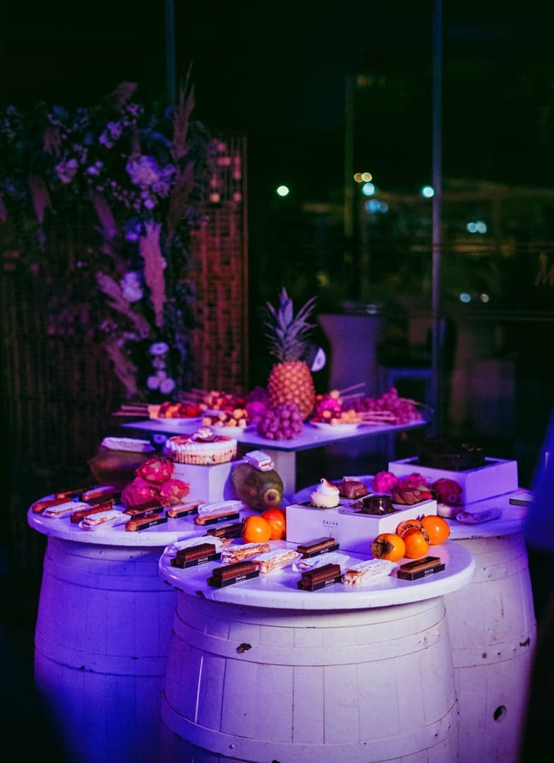 Een dessertbuffet in avondlicht met tropisch fruit en pralines op witte vaten.